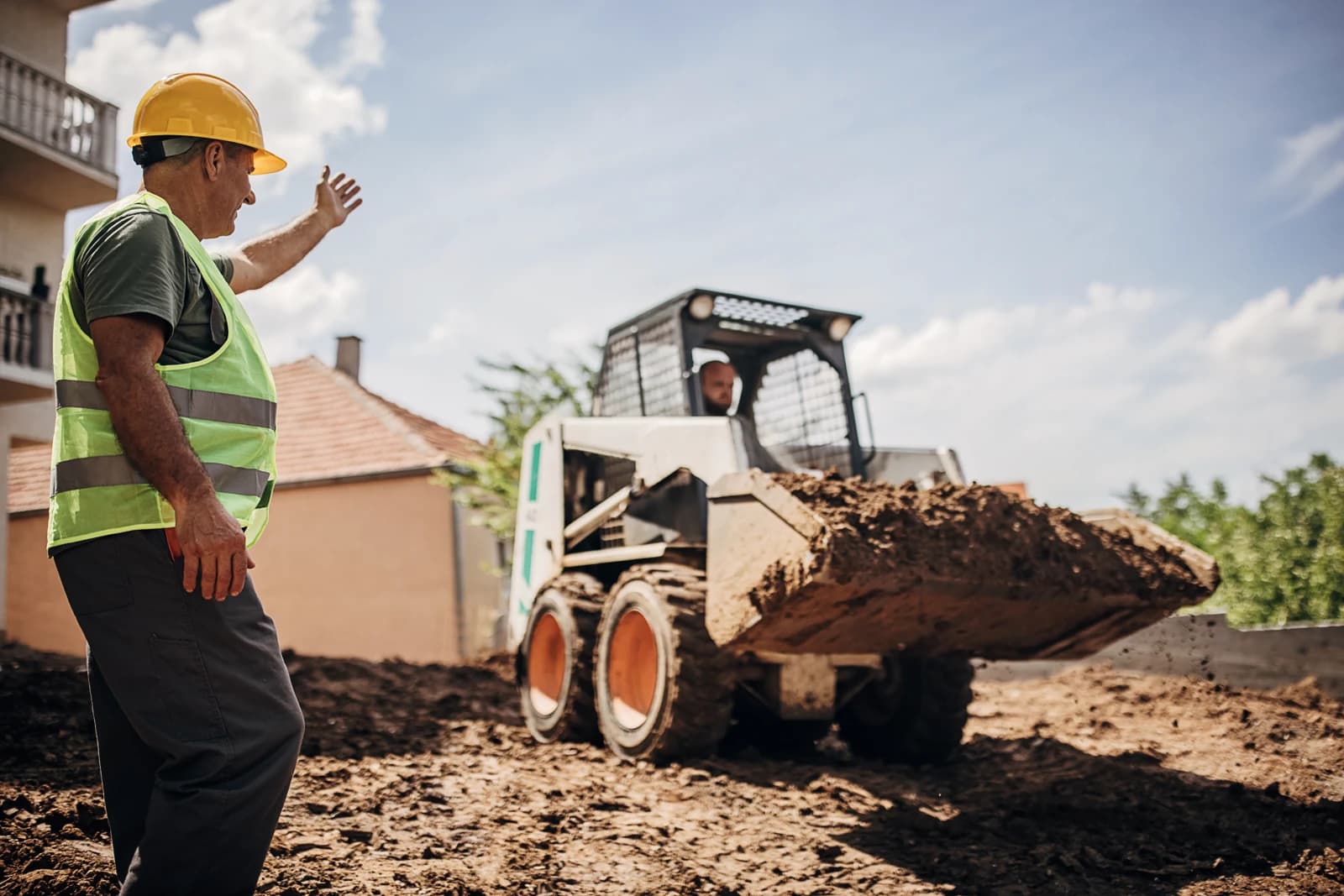 Site supervisor directing a skid steer operator on a job site